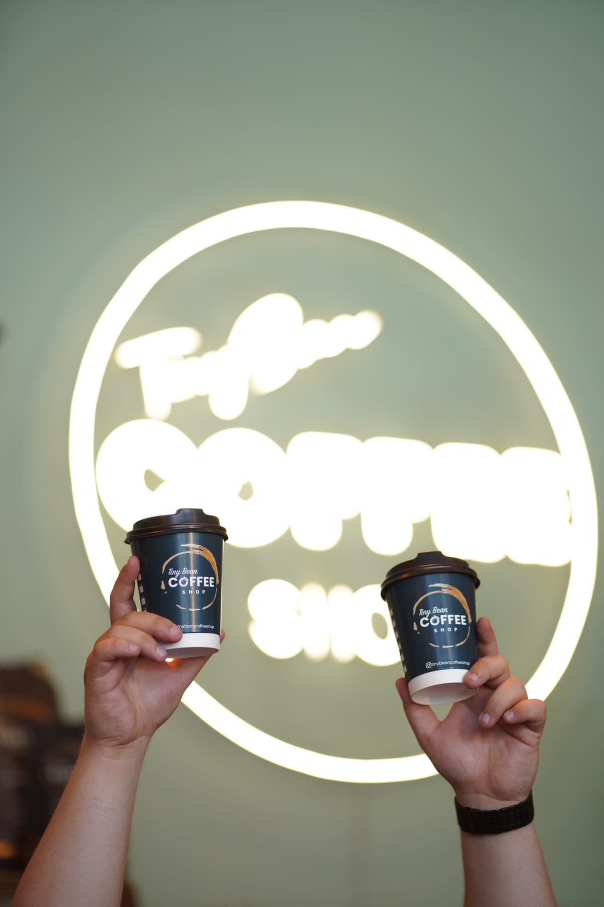 Tiny Bean kağıt bardaklarıyla kupa tokuşturma, neon logo önünde
